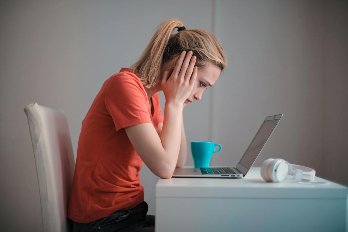 Woman with head in her hands leans over a desk with a laptop in front of her