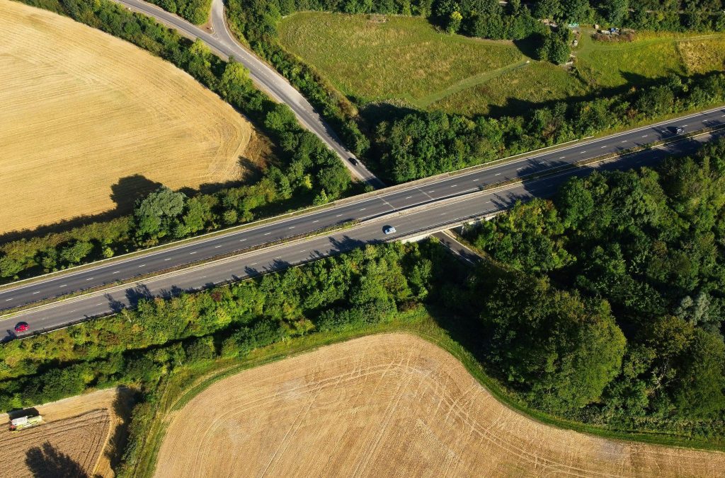 Aerial shot of a car driving on an empty main road between open fields in Bedfordshire, England.